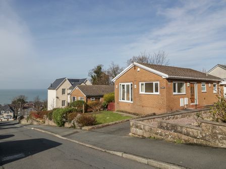 A street view with a brick house and other houses overlooking the sea at Arwelfa in Penmaenmawr