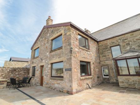 An outdoor patio area with stone walls and a table with chairs at Changing Tide in Beadnell