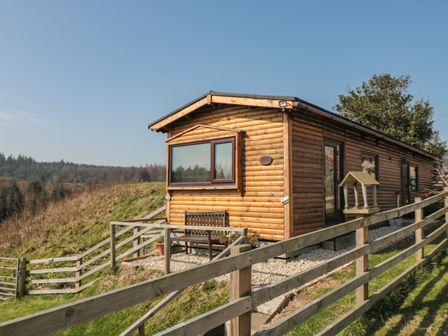 A wooden cabin with a bench outside and a fenced grassy hill at Castle View Cabin in Cloughton