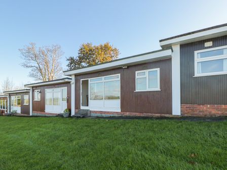 A view of a brown exterior wall with white framed windows and doors on a building with grassy lawn in front at 304 Norton Park in Dartmouth