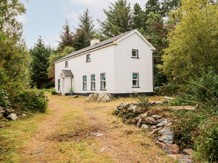 A white two-story house surrounded by trees with a driveway and stone wall at Kealduff Lower in Glenbeigh County Kerry