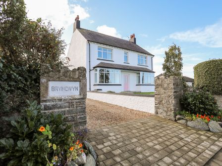A detached two-story white house with a pink door and garden with stone pillars at Bryngwyn in Trearddur Bay