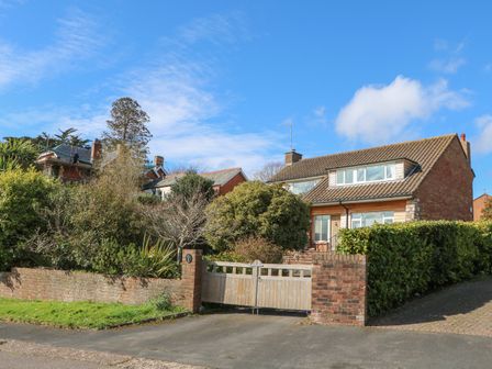A house with a tiled roof behind a wooden gate and brick wall with shrubs and trees at Casalmare in Exmouth
