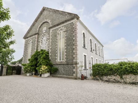 An exterior view of a stone and white building with arched windows and greenery at Capel Mawr Basement 19 Llanrug