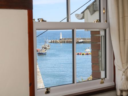 A window view of a harbor with boats and a lighthouse at Polkirt Forge in Mevagissey