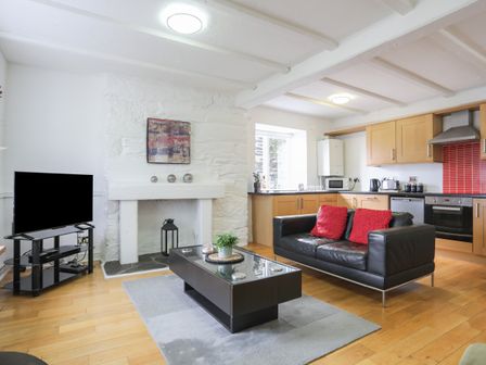 A living room with a black sofa with red cushions a black coffee table a television on a stand and a kitchen area at The Old Cornhill in Porthmadog