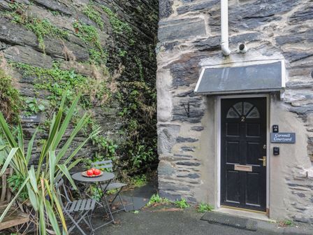 An outdoor courtyard area with a black door numbered 2 a small table with three chairs and three red apples on the table at Cornhill Courtyard in Porthmadog