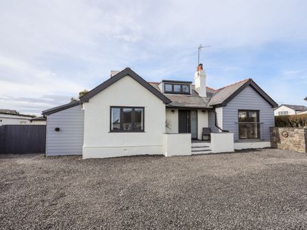 A single story house with white and gray exterior walls and a gravel driveway at Laneton in Rhosneigr