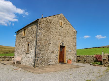 A stone house with wooden door and bench outside in a rural area at Field Barn in Alston