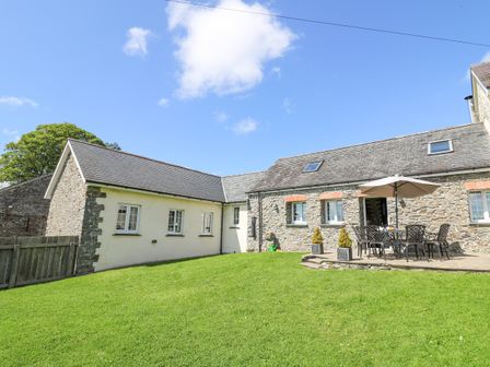 A stone and plaster house with patio furniture and an umbrella on the lawn at Yr Hen Beudy in Capel Bangor