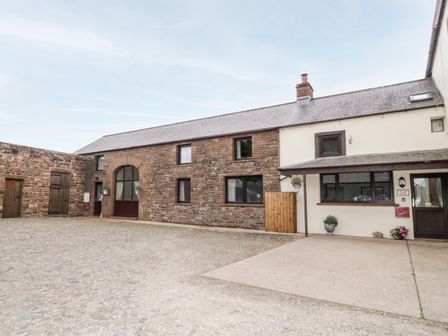 A courtyard with a stone and white building and wooden doors at The Old Cook House in Catterlen near Penrith