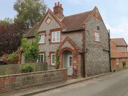 A stone and brick house with arched doorways and windows beside a street with plants at Compass Cottage in Bodham near Sheringham