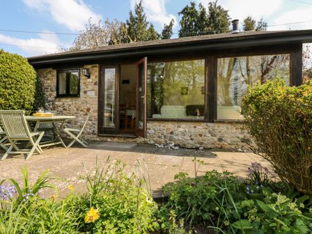 An outdoor patio with a table and chairs in front of a stone cottage with large windows and a glass door at Puffin Cottage in Hawkchurch