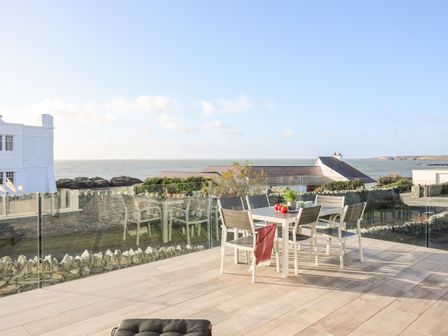 An outdoor patio with a dining table and chairs overlooking a sea view at Bryniau in Trearddur Bay