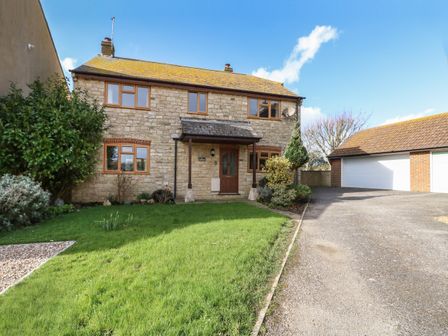 A stone house with brown framed windows a wooden door and a green lawn with bushes at Gabrianne in Burton Bradstock