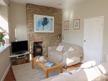 A living room with a stone fireplace a TV on a corner shelf and two sofas at 1 Bailey's Cottage in Stoke Fleming