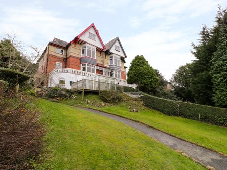 A multi-story brick house with a sloped grassy lawn and a paved path at Preswylfa in Caernarfon