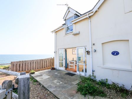 A white house with open French doors leading to a dining area and a stone patio overlooking the sea at The Reach in Hallsands