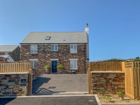 A stone house with a grey roof and blue front door with driveway and wooden fencing at Beacon House in St Agnes