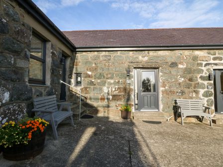 An outside stone wall with three gray doors two gray benches and flower pots at Tyddyn Sianel - Celyn in Llanystumdwy near Criccieth