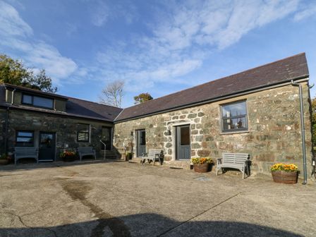 A stone building with wooden benches and flower pots outside at Tyddyn Sianel - Derw in Llanystumdwy near Criccieth
