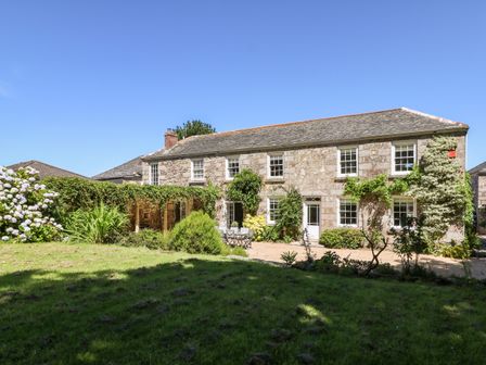 A stone house with green plants and a patio set in a garden at Culdrose Manor in Helston