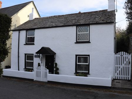 A white cottage with black trim windows and two white gates at Hawthorn Cottage in St Teath
