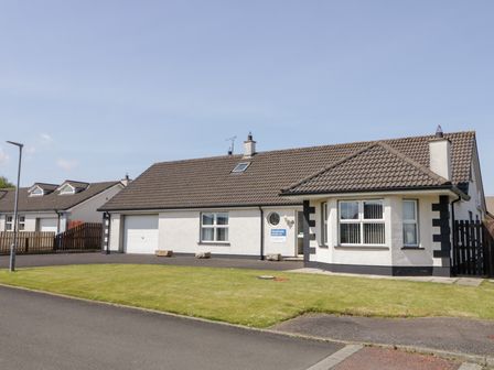 A detached house with a tiled roof a garage and a lawn at SeaShells in Castlerock