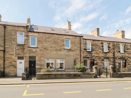 A row of stone terraced houses with front doors and small fenced gardens at The Old Sweet Shop in Alnwick