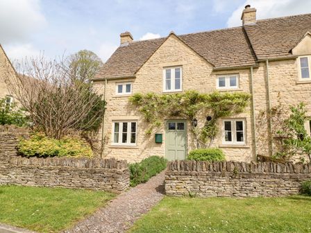A stone cottage with green door and windows surrounded by a stone wall and garden path at 3 Painters Field in Quenington Near Cirencester
