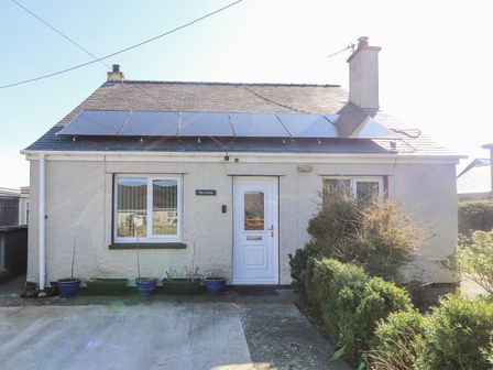 A front view of a house with solar panels on the roof and plants in pots outside at Tanyfron Holiday Studio in Bryngwran near Gwalchmai