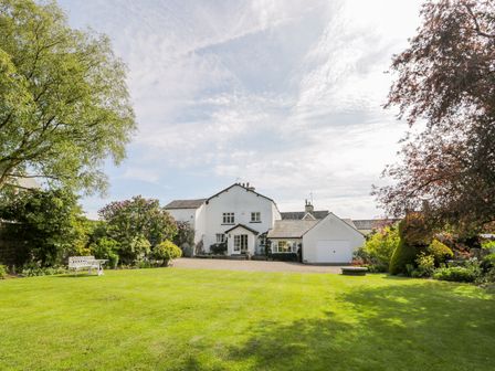 A white house with a garage surrounded by a large lawn and trees at The White House in Cartmel