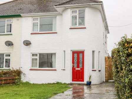 A white semi detached house with a red front door and lawn at Cranberry in Bude