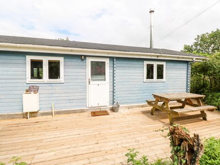 An exterior of a blue wooden cabin with white door and windows and a wooden picnic table on a deck at The Beach Shack in Llansteffan