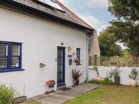 The exterior of a white house with blue window and door frames with plants and a small garden area at The Granary in Rhoscolyn