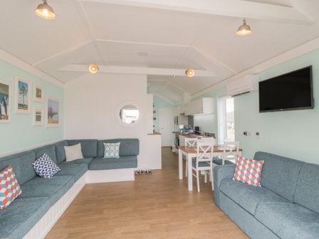 A living room with blue sofas and a dining table next to a kitchen with white cabinets at Shore Thing 280 in Wilsthorpe
