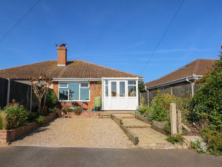 A single-story house with a tiled roof a small front porch a gravel driveway and a garden on both sides at Honeybees Haven in Hunstanton
