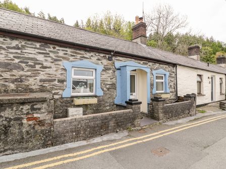 Stone cottage with blue window frames and entrance along a street with double yellow lines at Crud yr Awel in Braichmelyn near Bethesda