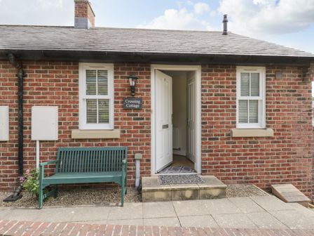 The front exterior of a brick cottage with two windows a green bench and an open white door at Crossing Cottage Whitby