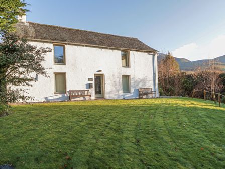 A white two-story house with a slate roof and two wooden benches on a lawn at Low Melbecks House in Bassenthwaite near Keswick