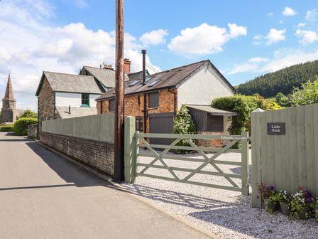 A gated entrance to a brick and plaster house with gravel driveway and flowers on a fence at Little Nook in Llandrillo