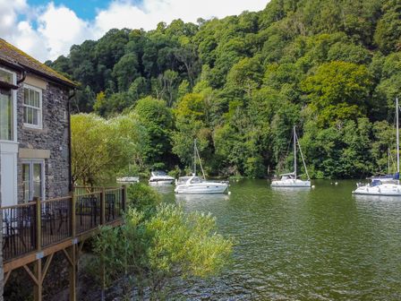 A stone house with a wooden deck overlooking boats on a river with trees in the background at Lund Far Sawrey