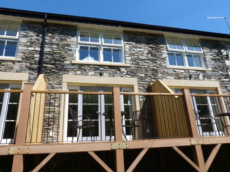 A stone exterior of a building with wooden balcony and metal chairs at Frost in Far Sawrey