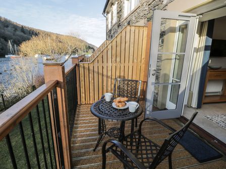 A balcony with a small table and two chairs overlooking a lake with boats at Pennington in Far Sawrey