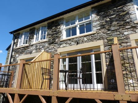 A stone exterior of a building with white framed windows and a wooden balcony with metal chairs at Pearsall in Far Sawrey