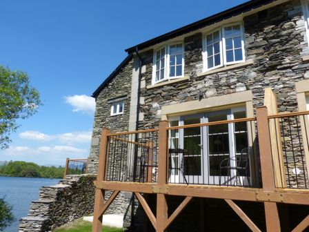 A stone house with a wooden balcony overlooking a lake at Lowe-McConnell in Far Sawrey