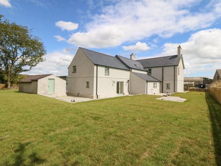 A two story house with an adjacent small building on a grassy lawn under a partly cloudy sky at Trewen in Botwnnog near Sarn Meyllteyrn