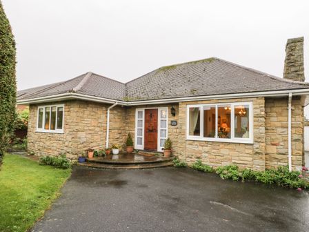 The exterior of a stone house with a wooden front door potted plants and windows showing interior lights at Sanderling in Scalby