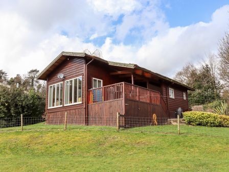A wooden cabin with a deck and fencing on a grassy hill at Watersview Lodge in Rudyard near Leek