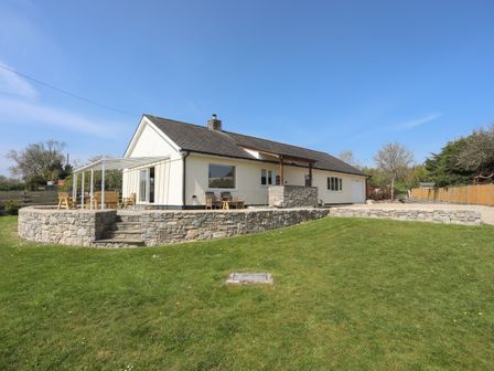A bungalow with a stone terrace and lawn in a rural setting at Cae Capel in Pentraeth